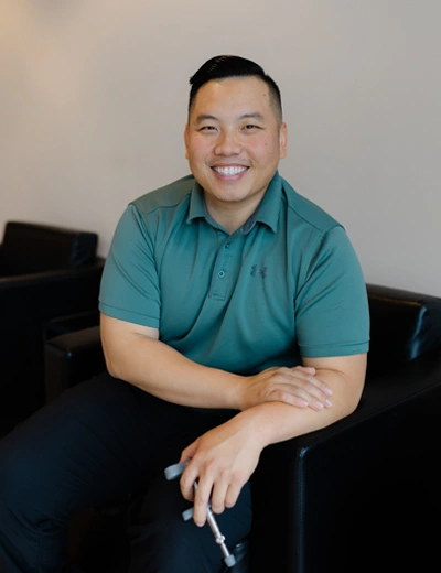 Gene Xiong smiling while sitting in a black leather chair.
