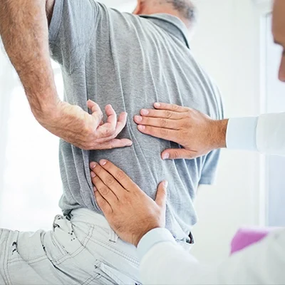 Person receiving a physical examination for lower back pain, with a healthcare professional pressing on the back area